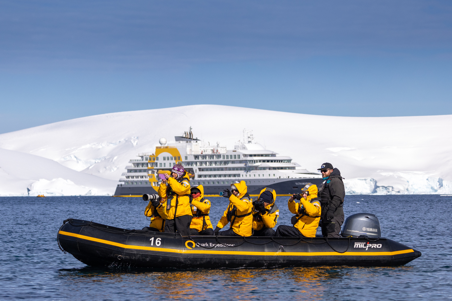 Guests in yellow expedition parkas photograph from a Quark Expeditions Zodiac with Ultramarine anchored beside a snow-covered Antarctic island