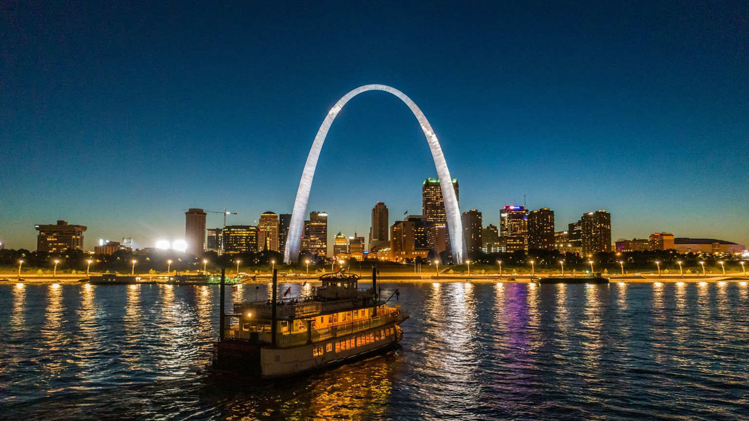 Gateway Arch and St. Louis skyline at night reflected on the Mississippi River with a riverboat in the foreground