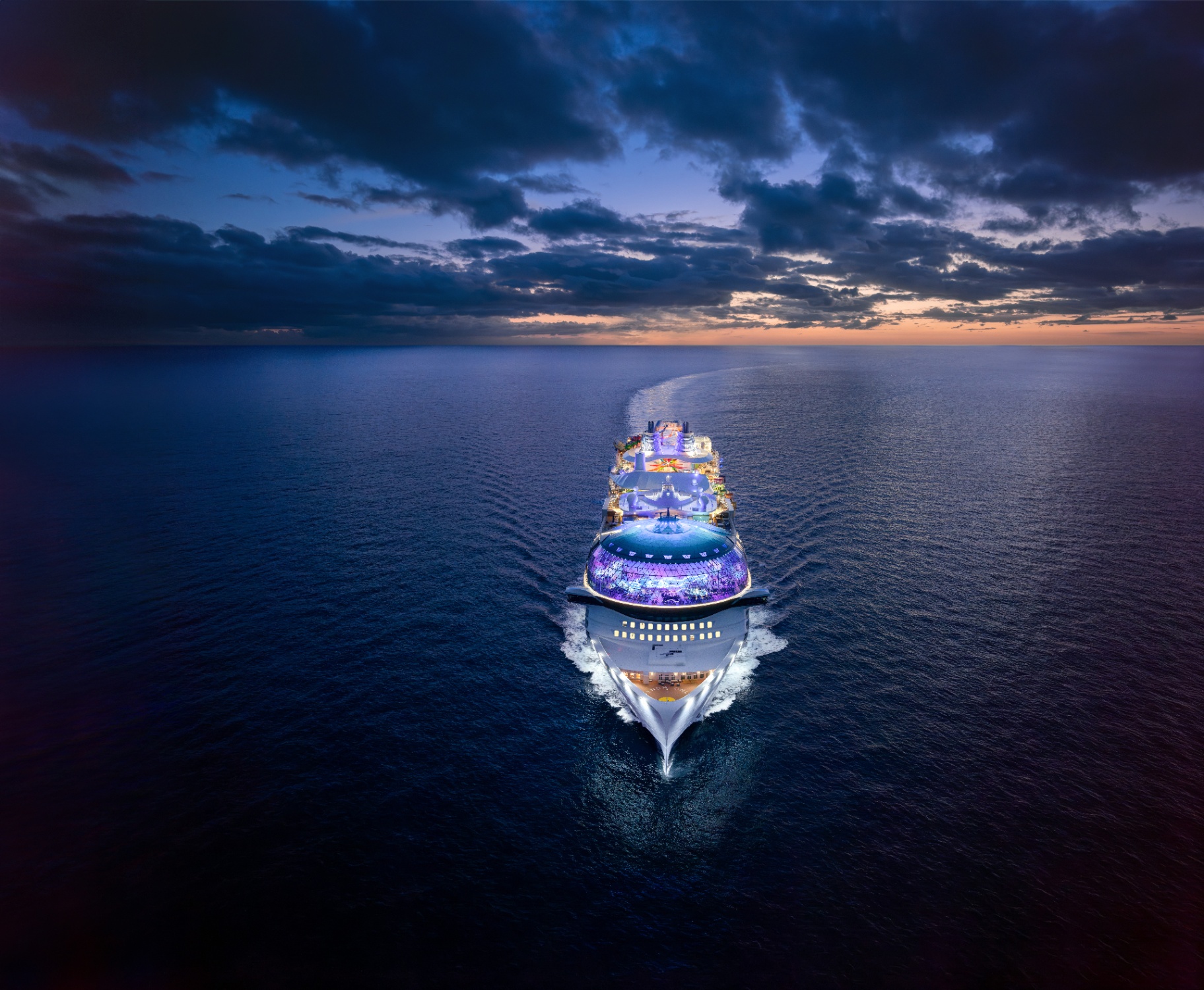 Aerial view of Royal Caribbean's Icon of the Seas sailing at twilight with an illuminated wake